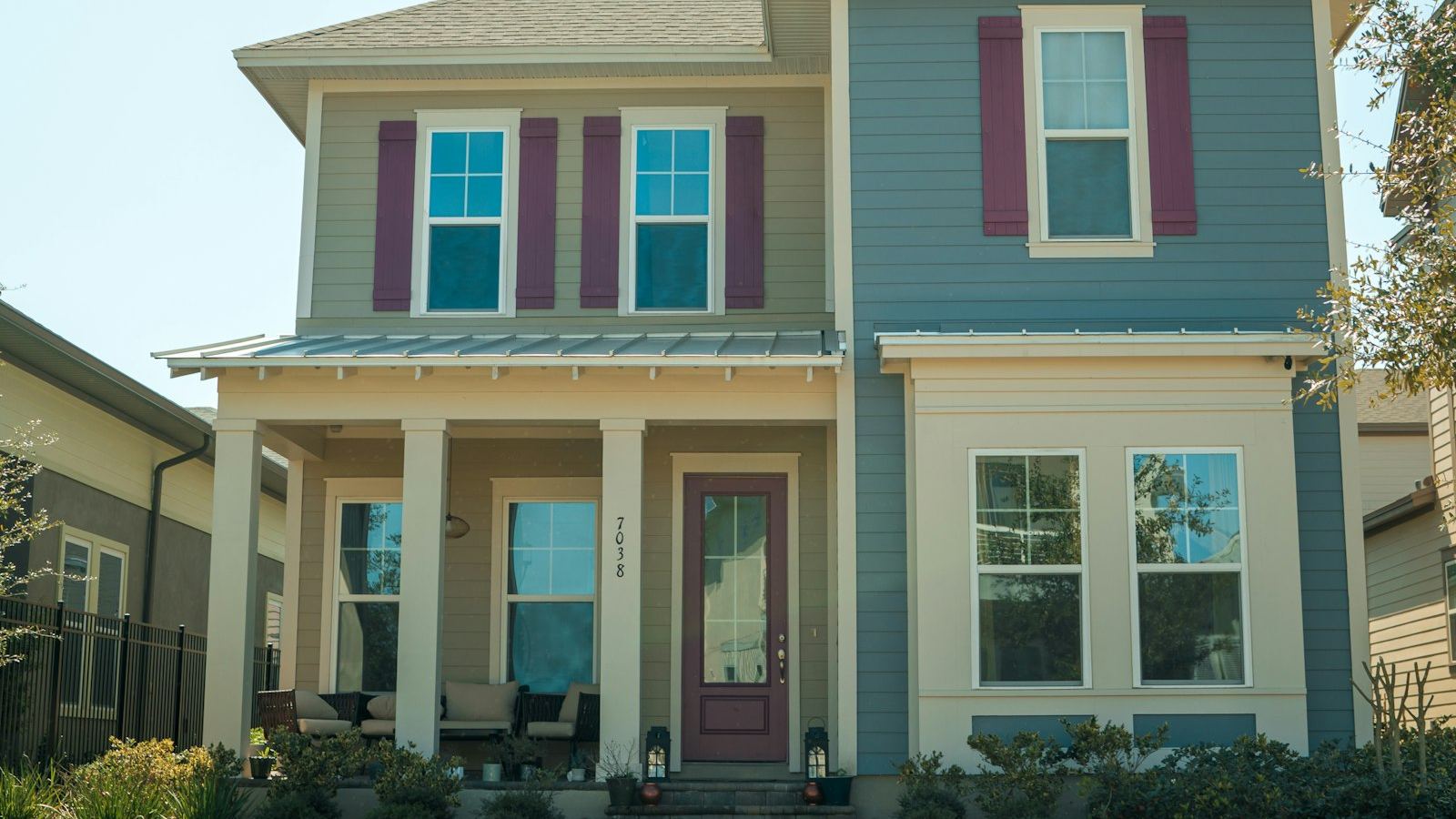 Two-story house with blue and tan siding and red shutters on a sunny day