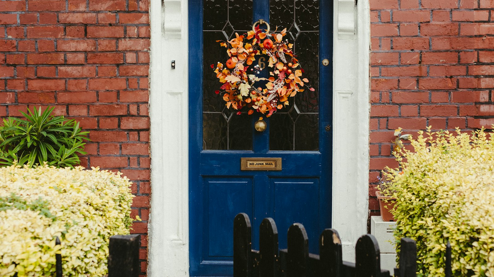 Blue front door with a fall wreath on a brick house